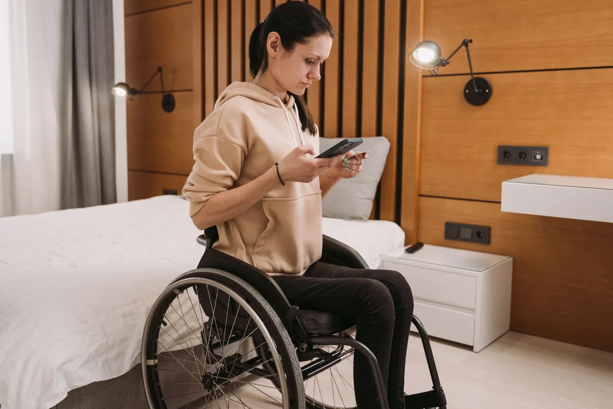 Mujer en silla de ruedas junto a la cama de una habitación
